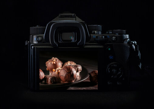 DSLR camera or mirrorless body lit by a rim light showing chocolates on the back of the camera display. Low key light photography