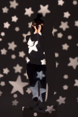 A monochrome soft portrait of a little girl in jeans and a white sweatshirt standing against the wall in a light in a dark room. The girl is smiling on an isolated background. Selective focus