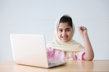 muslim girl using a laptop computer and raised hand for celebrating good news on the table