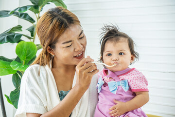 Mother feeding her baby daughter with spoon. Mother giving healthy food to her adorable child at home, Baby food.