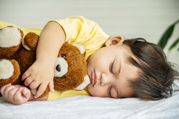 Cute,Portrait of little infant or baby sleeping on bed with comfort, She is sleeping with teddy bear in an embrace, Adorable newborn kid concept