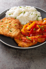 German schnitzel served with paprika sauce and rice close-up in a plate on the table. vertical