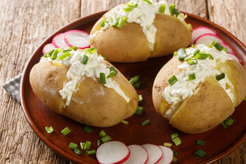 Delicious potatoes with cottage cheese, sour cream and green onions close-up in a plate on a wooden table. Horizontal