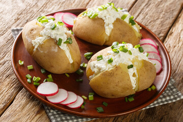 Homemade potatoes stuffed with salted cottage cheese, sour cream and green onions close-up in a plate on a wooden table. Horizontal