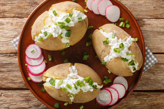 Homemade potatoes stuffed with salted cottage cheese, sour cream and green onions close-up in a plate on a wooden table. Horizontal top view from above