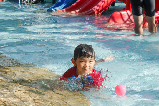 Portrait image of 4-5 years old baby. Happy Asian child girl swimming and play water in the blue pool. She smile and laugh. Summer season.