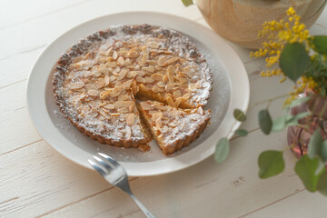 Homemade almond tart on a white plate with folk and knife.