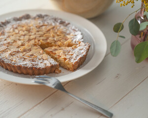 Homemade almond tart on a white plate with folk and knife.