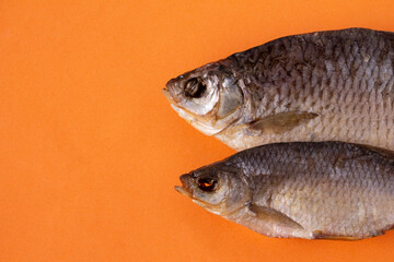 two dried fish on orange background, copy space