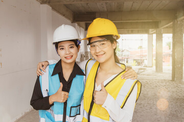 Two young engineers architects and beautiful asian workers work together on the construction site wearing helmets and safety vests : Two young asian workers smiling looking camera with thumbs up.