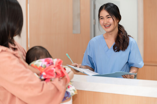 Happy Nurse Talking With Mom And Baby At Counter At Hospital