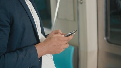Close up businessman standing on the seat using modern smartphone to internet checking news on electric train, Passenger young man commuting texting on mobile phone by railway transport