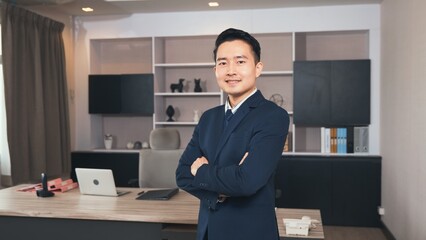 Businessman leader smiling in formal suit glasses standing smart with his arms crossed in an office workplace, portrait of happy young male boss manager or CEO look at camera