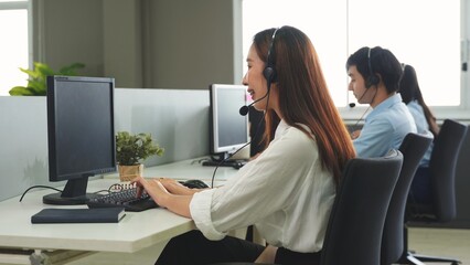 Call center young employee working with headset, Smiling customer support operator team at work surrounded by colleagues working in the office, Helpdesk customer services support agent concept
