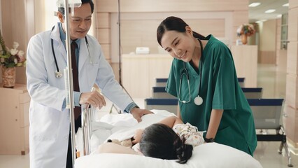Cute little sick girl patient lying in hospital bed talking with smiling doctor and nurse standing...