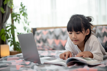 Little Asian girl using a laptop while lying on the bed