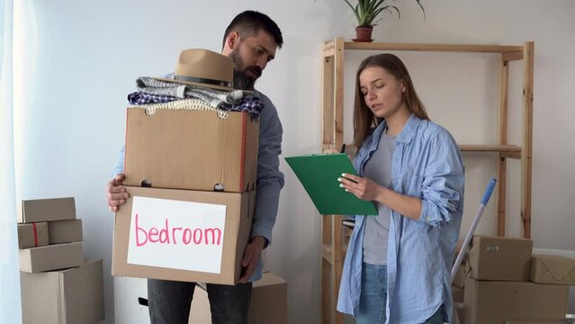 couple in love in a new empty apartment are standing. The man holds a box with things, the woman notes the presence in the list of things.