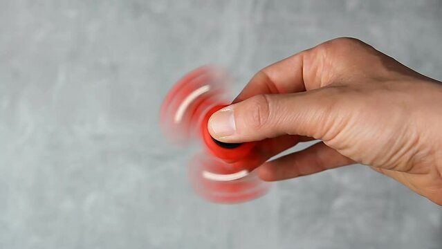 Man hand rotating red plastic fidget spinner on marble background. Anti stress toy
