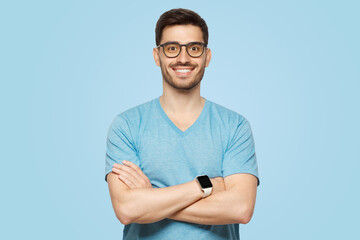 Young handsome man wearing blue t-shirt and smartwatch, standing with arms crossed