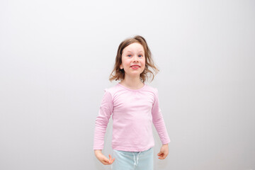 Girl, Caucasian 6 years old, in a pink coat on a gray background. The child is happy and smiling, emotions on his face.