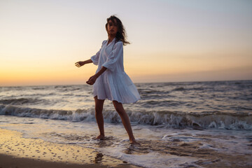 Stylish woman in elegant white dress posing near the sea. Summer time. Travel, weekend, relax and lifestyle concept.