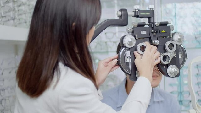 Young male customer being examined visual test using Bifocal Optometry eyesight measurement device by ophthalmologist in optical center, eyecare concept.
