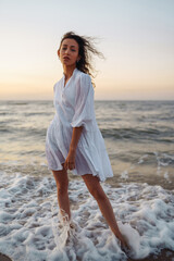 Stylish woman in elegant white dress posing near the sea. Summer time. Travel, weekend, relax and lifestyle concept.