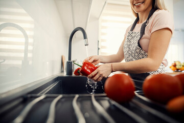 A housewife washing paprika in kitchen sink.