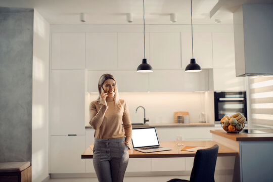 A Happy Entrepreneur Having A Phone Call In Kitchen At Her Home.