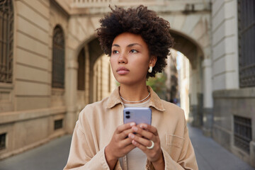 Attractive female model reads text message on smartphone strolls during walking tour outdoors has...