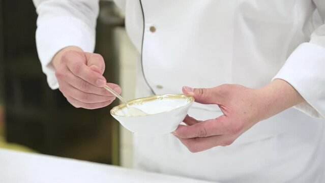 Closeup of a chef's hands stirring cream in a white china bowl. 120p footage.
