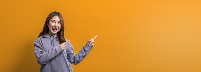 Portrait of Asian woman gesturing pointing at empty space for ad text, portrait concept used for advertisement and signage, isolated over yellow background, copy space.