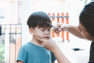 Asian mother cuts her son's hair by herself at home. Happy haircut ideas for kids. Mothers are happy to cut their children's hair.