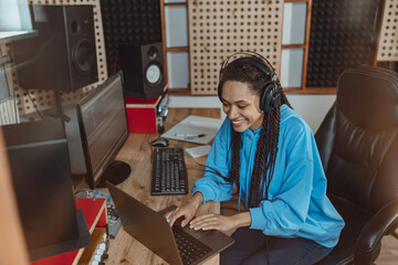 Cheerful African American female sound engineer working on laptop in the sound recording studio