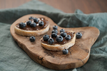 Organic chocolate hazelnut spread with fresh blueberries on ciabatta slices on wood board
