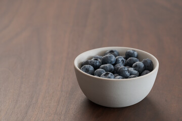 Fototapeta na wymiar Fresh washed blueberries in white bowl on walnut table