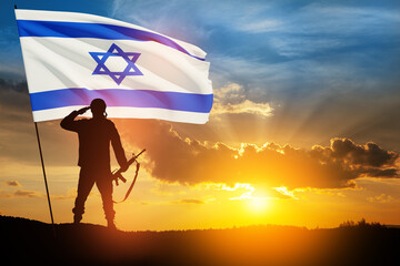 Silhouette of soldier saluting with Israel flag against the sunrise in the desert. Concept - armed...