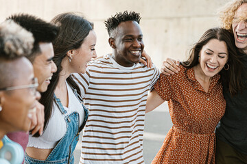 Group of happy multiracial young best friends laughing and having fun together - United millennial people hugging each other while hanging out enjoying free time at summer weekend - Friendship concept - obrazy, fototapety, plakaty