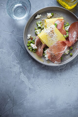 Grey plate with pea, ricotta and prosciutto open lasagna, above view on a grey concrete background, vertical shot, copy space