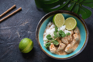 Thai red chicken curry with coconut milk and white rice, elevated view on a dark-brown stone background, horizontal shot