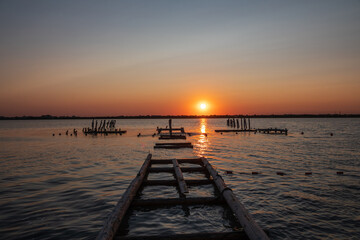 Obraz premium Beautiful red and orange sunset over the sea. The sun goes down over the sea. A flock of cormorants sits on a old sea pier in orange sunset light