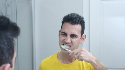 dark-haired young man in yellow t-shirt brushing teeth in bathroom