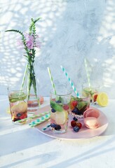 Refreshing detox drinks from organic fruits, berries, citruses and mint leaves in glasses, a bouquet of flowers on the kitchen table, healthy food, vitamin water