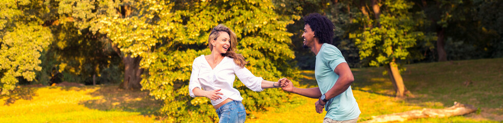 Young happy couple running on the meadow while holding hands on a sunny summer day