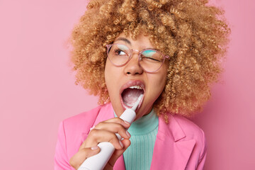 Teeth care and daily routines concept. Curly haired woman brushes teeth with electric toothbrush...