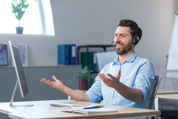 Happy businessman with headset for video call working in modern office, smiling man looking at computer monitor