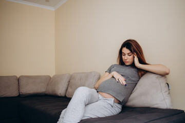 Obraz premium Pregnant woman with hand on forehead suffering headache sitting on a couch in the living room at home