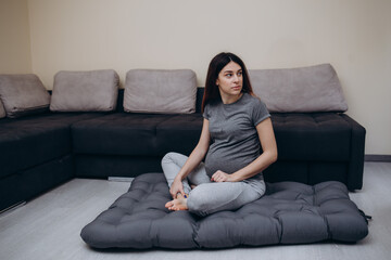 Fototapeta premium Beautiful happy pregnant african woman hugging her tummy, sitting on sport mat, enjoying her pregnancy, free space