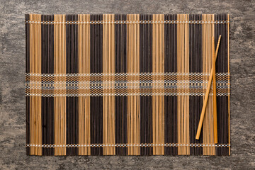 Two chopsticks and bamboo mat on cement background. Top view, copy space