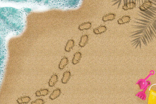 Footprint on sandy beach, walking on sand concept, palm shadow and sea wave and toys composition, top view of sand beach, summer times trip idea